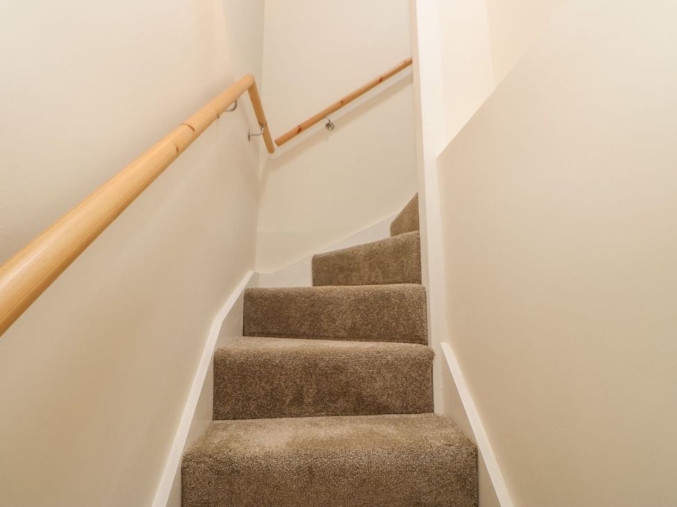A staircase with carpet and wooden handrail at Dairy Cottage in Kirkby Stephen