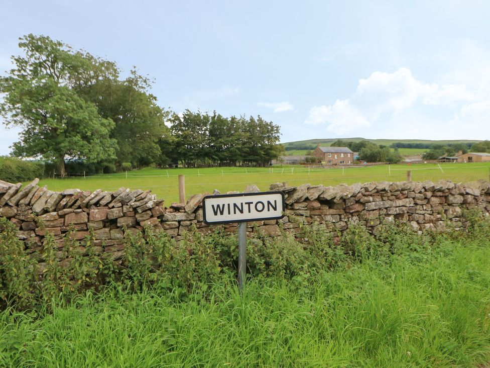 A sign indicating Winton with a house and trees in the background at Dairy Cottage Kirkby Stephen