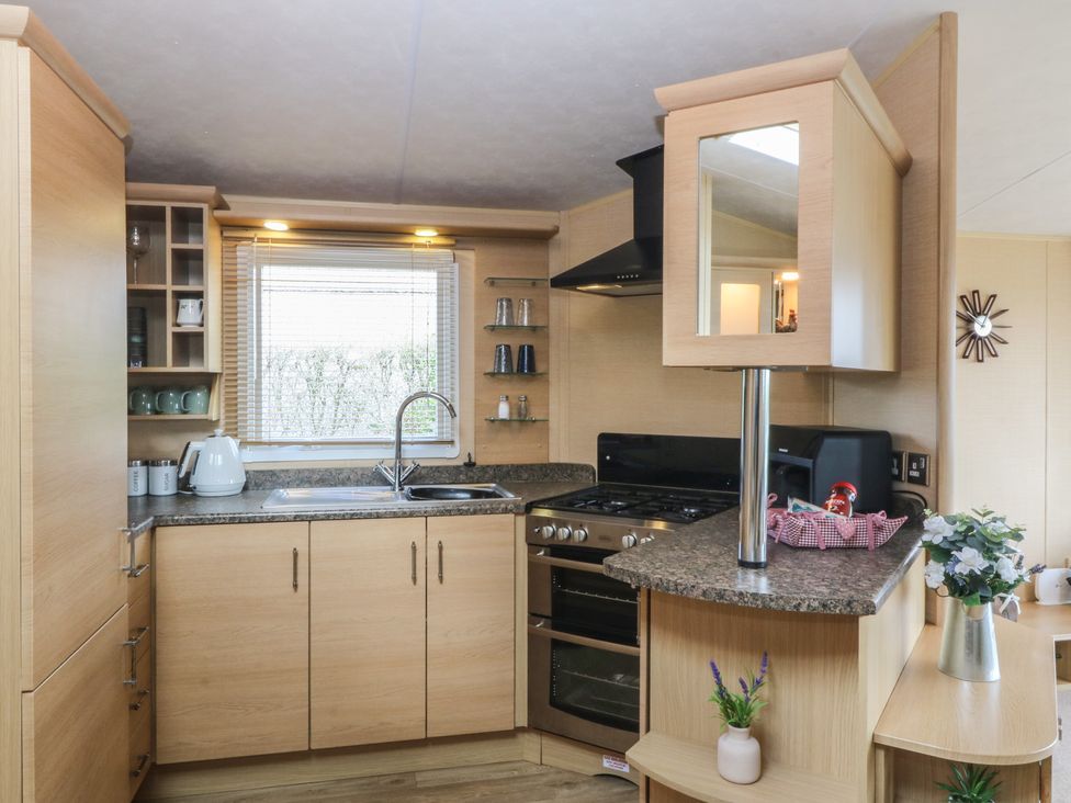 A kitchen with cabinets, sink, stove, and microwave at Temperance Caravan in Trefor near Bodedern