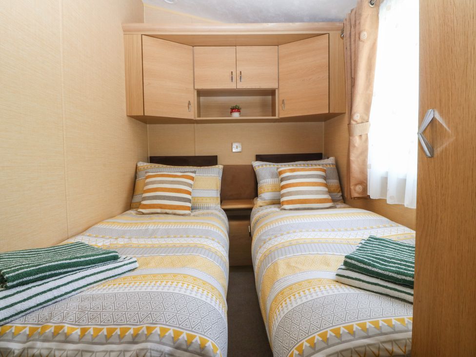 A bedroom with two single beds and a shelf unit at Temperance Caravan, Trefor near Bodedern