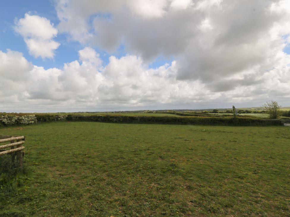 A grassy area with a fence and cloudy sky at Temperance Caravan Trefor near Bodedern