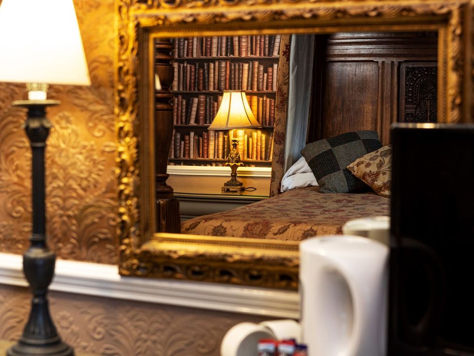 A bedroom with a lamp and a mirror reflecting a bookshelf at Lonsdale House Bowness-On-Windermere
