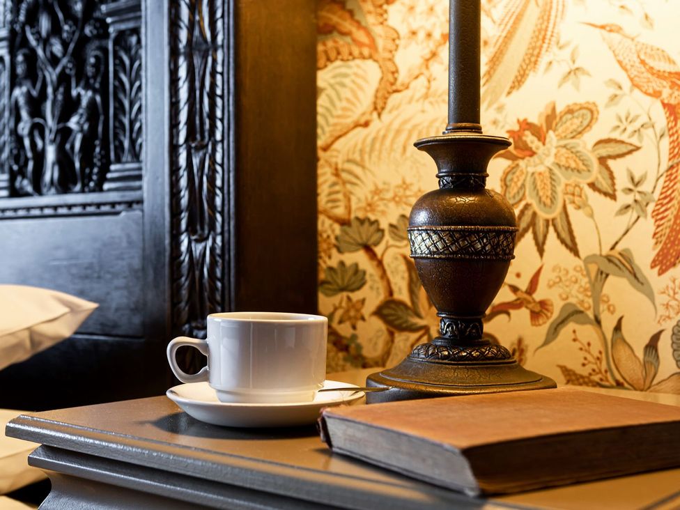 A bedside table with a coffee cup, lamp, and book at Lonsdale House Bowness-On-Windermere