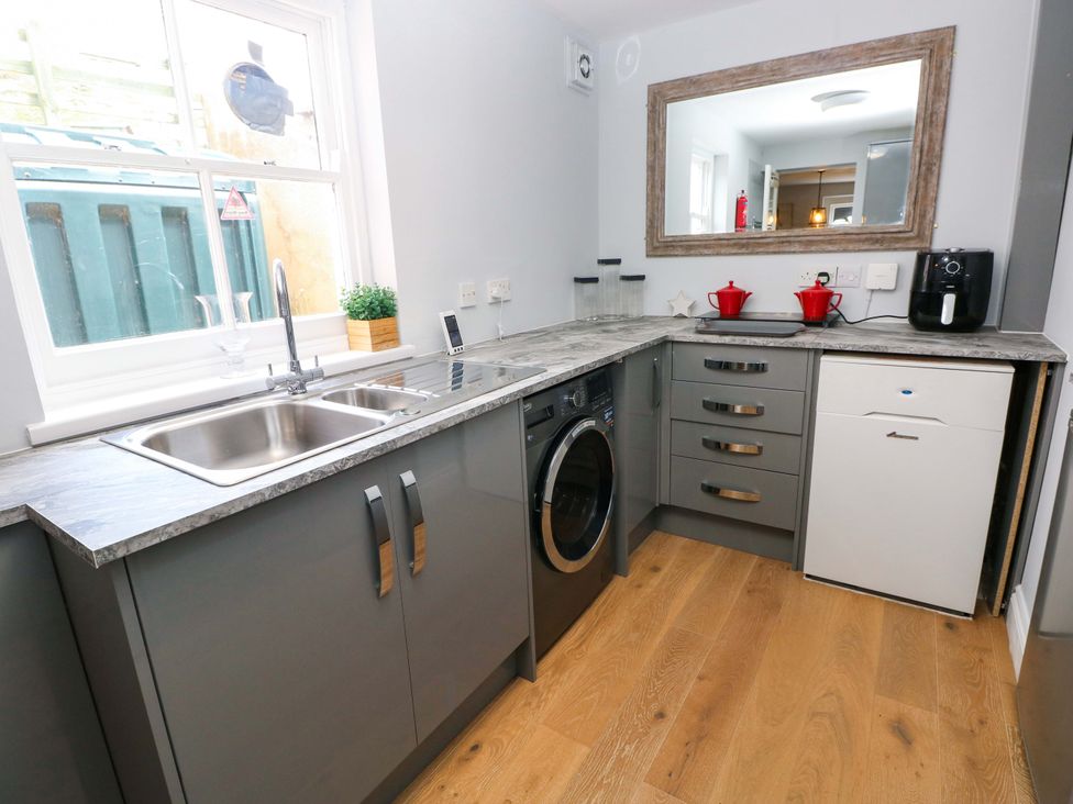 A kitchen with a sink, washing machine, and mirror at Newgale Cottage in Haverfordwest