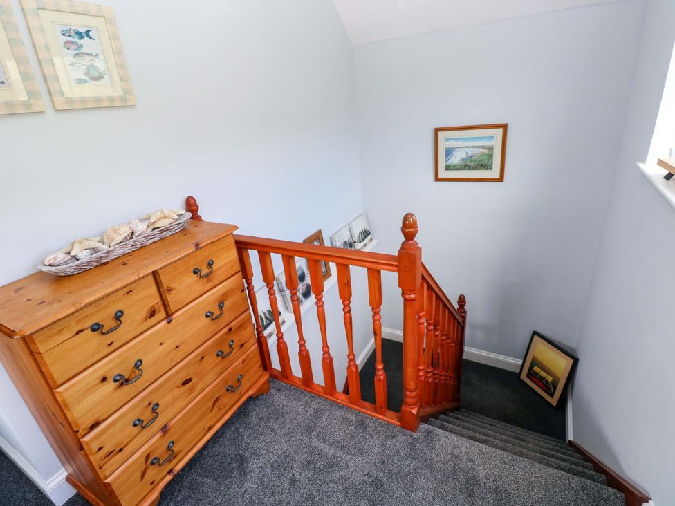 A staircase with a chest of drawers and pictures at Newgale Cottage in Haverfordwest