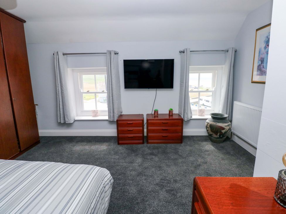 A bedroom with a bed, wardrobe, television and windows at Newgale Cottage in Haverfordwest