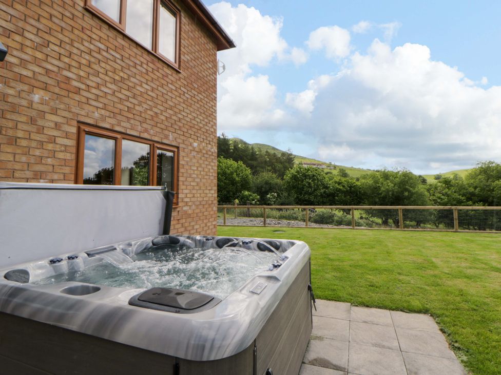 A hot tub beside a brick wall with windows in an outdoor area at Yr Onnen 