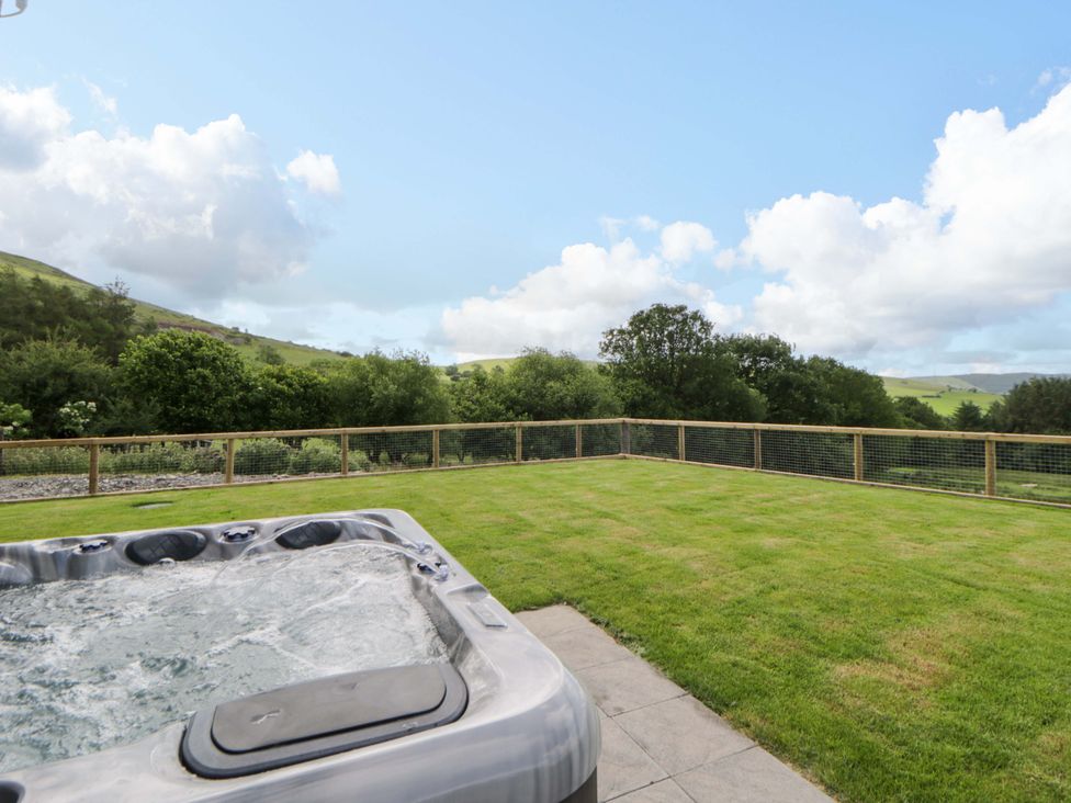 A hot tub on grass with a fence and countryside view at Yr Onnen