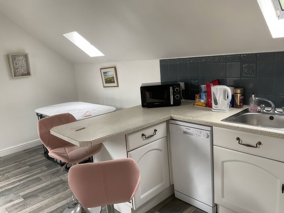 A kitchen with a microwave, kettle, dishwasher, and bar stools at The Cottage in Stokesley