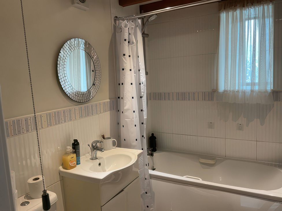 A bathroom with a bathtub, sink, and mirror at The Cottage in Stokesley