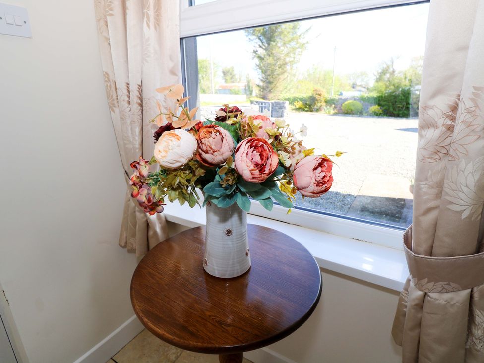 A vase with flowers on a table beside a window at Cahir Cottage Ballinrobe, County Mayo