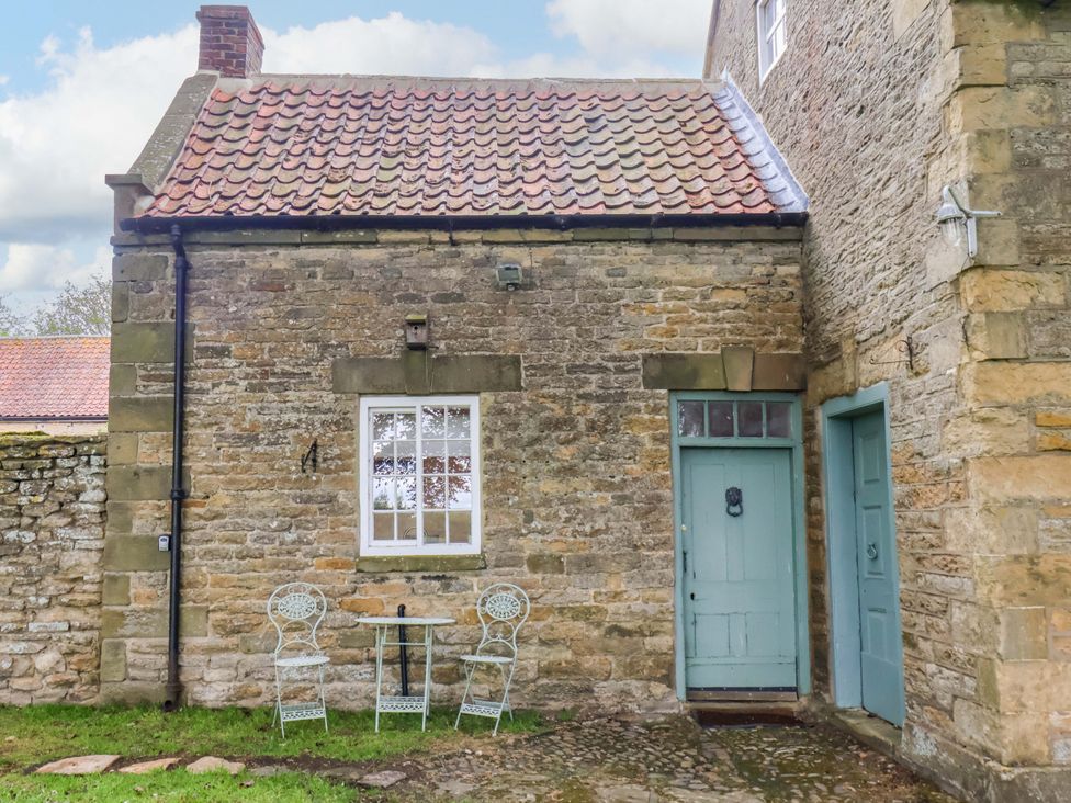 An exterior view of a stone cottage with seating at The Gardener's Cottage, Low Hall Scarborough