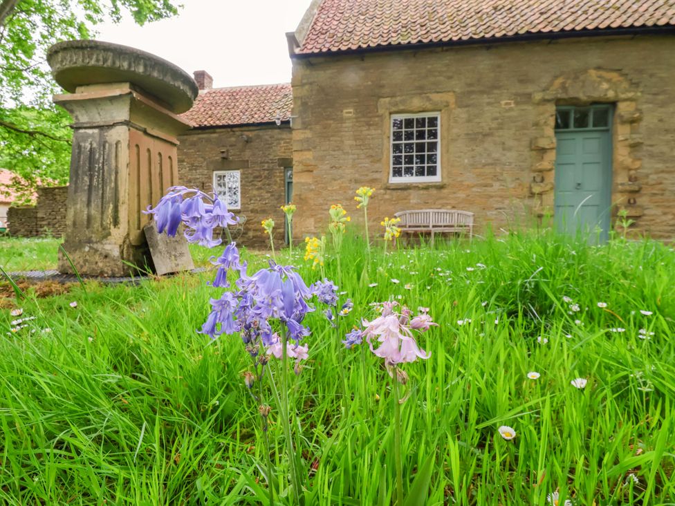 An outdoor area with flowers and a bench near a stone house at The Gardener's Cottage, Low Hall Scarborough
