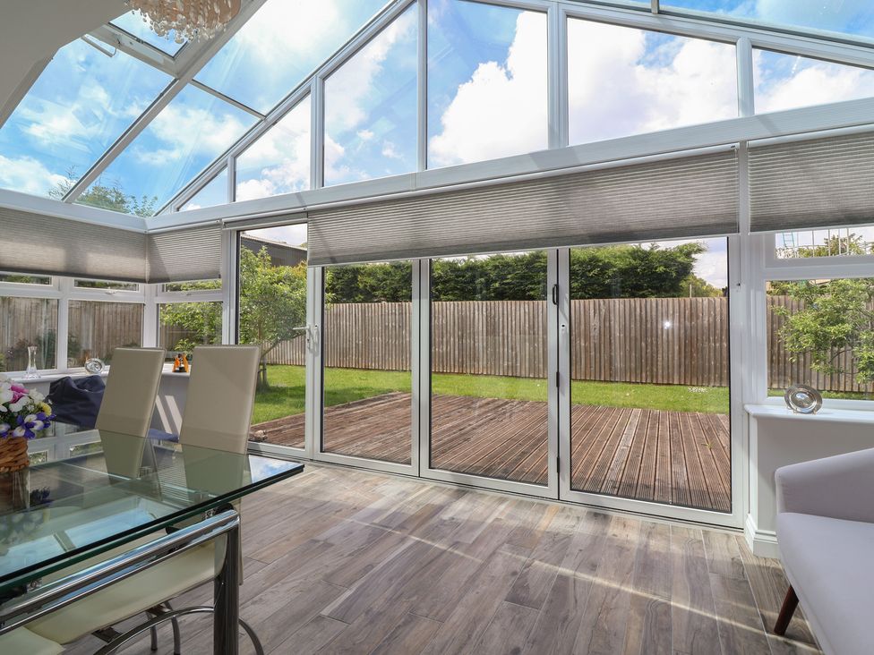 A conservatory with a dining area and sliding doors leading to a garden at Villina Somerton
