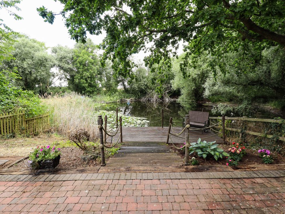 A garden with a wooden dock and seating overlooking water at Willow Tree Barn Spalding