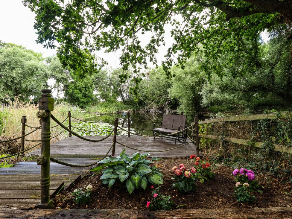 A wooden deck with a bench and flower bed near water at Willow Tree Barn in Spalding