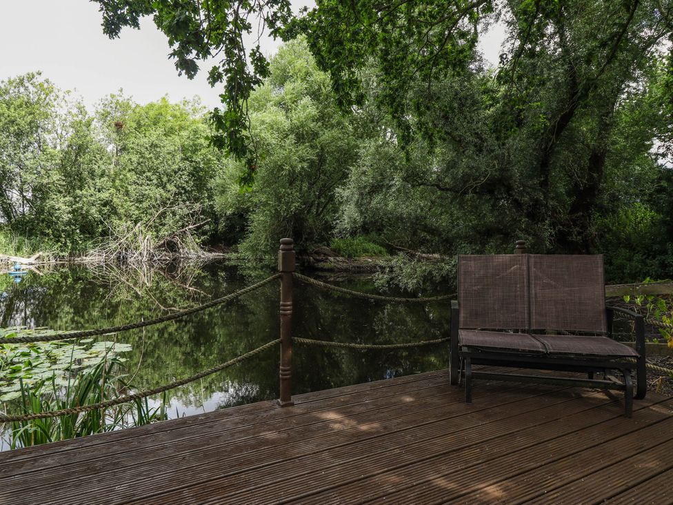 A bench on a wooden deck near water and trees at Willow Tree Barn in Spalding