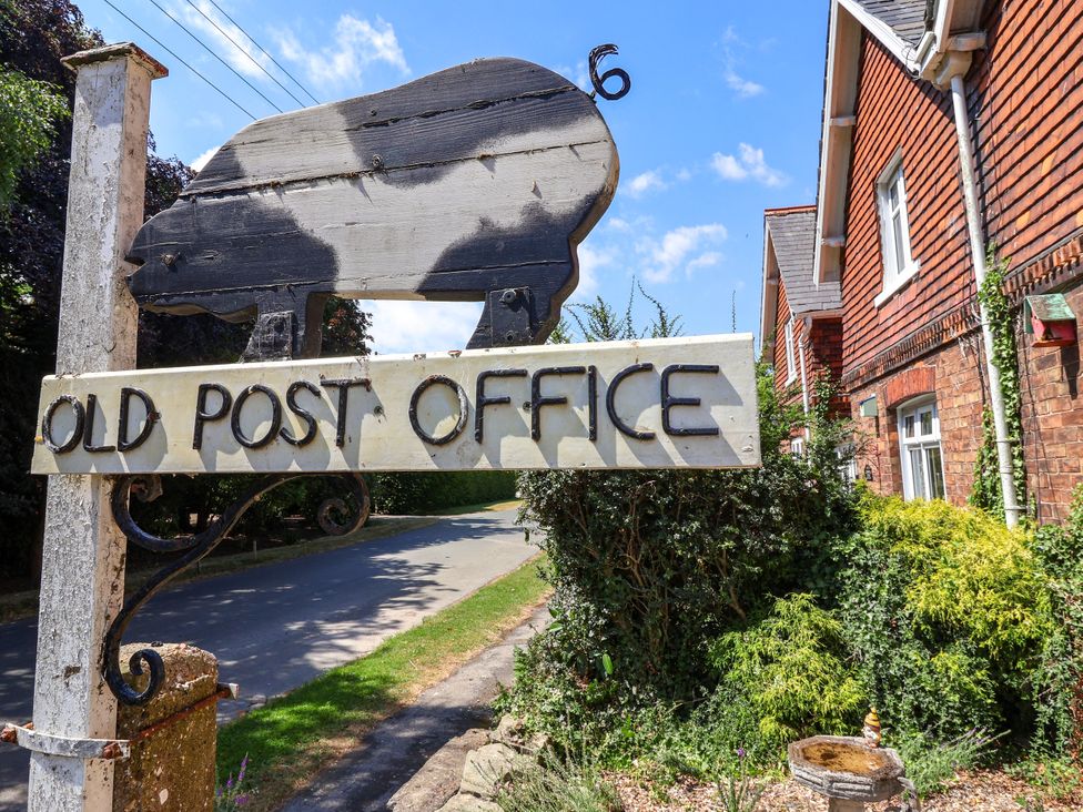 A sign for the Old Post Office on a street with bushes at Old Post Office