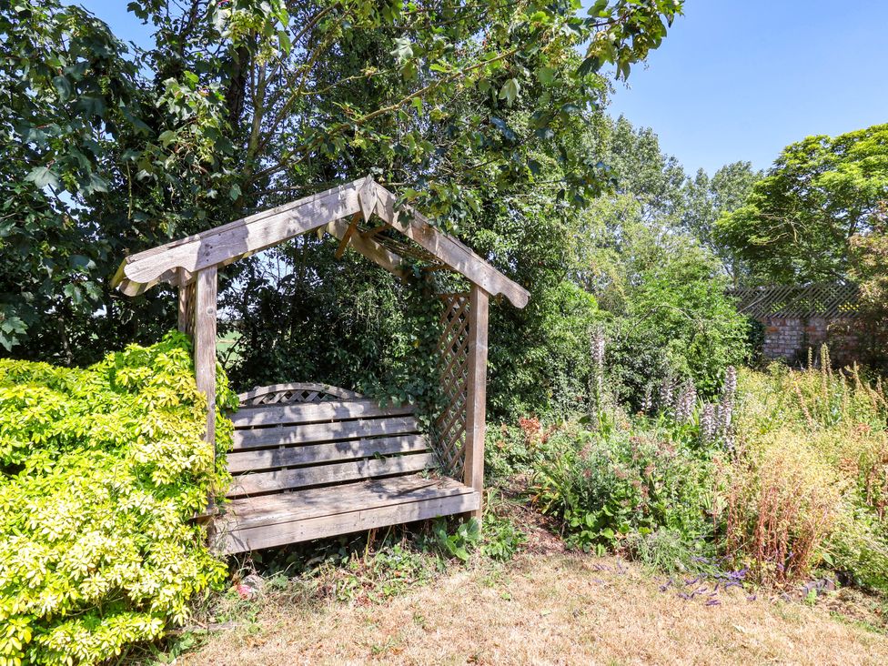 A garden with a wooden bench swing surrounded by greenery at The Old Post Office