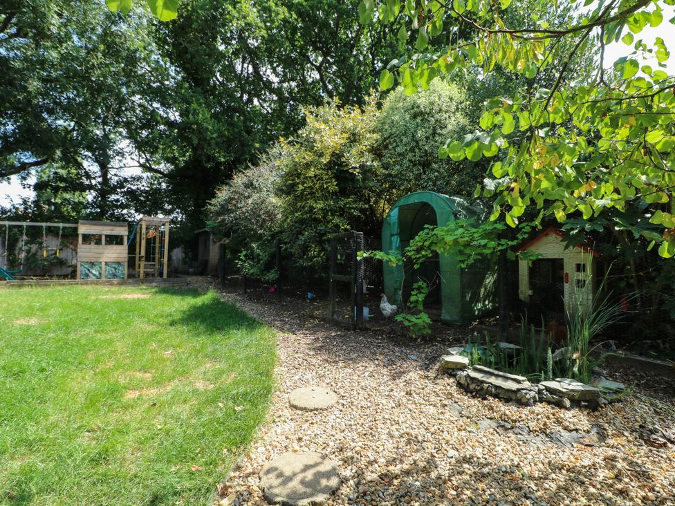 A garden with grass, a playhouse, and various plants at Taliesin in Hailsham