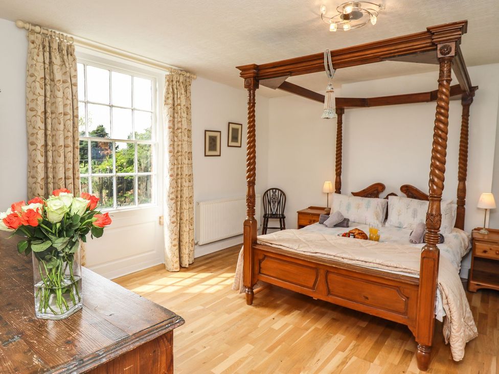 A bedroom with a four-poster bed and a vase of flowers at Reighton House in Filey