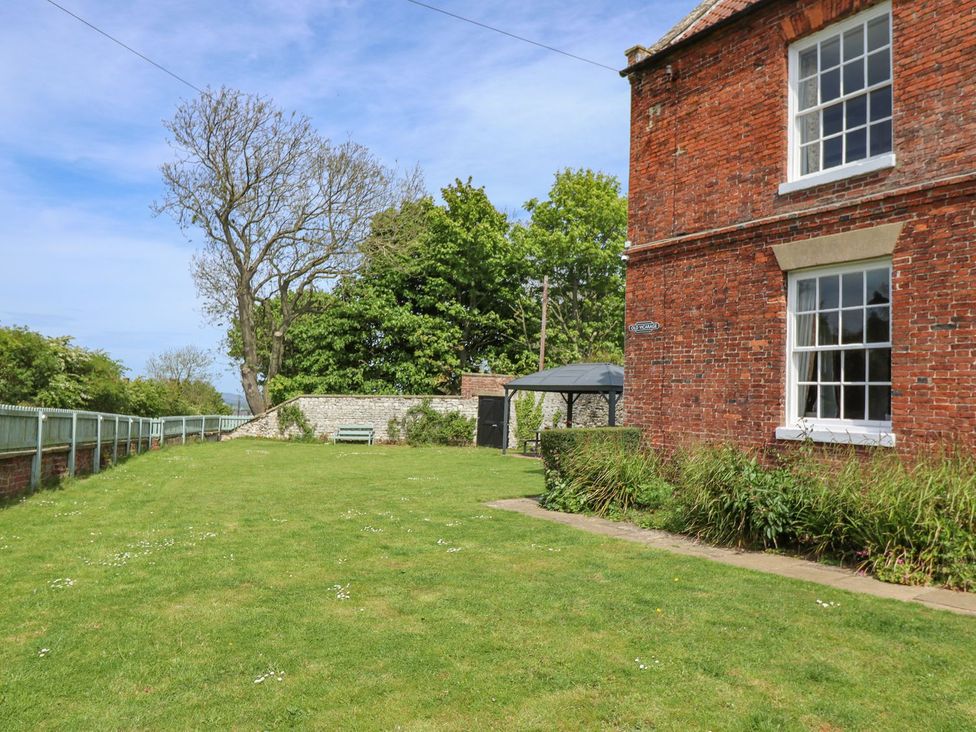 A garden with grass, trees, and a bench at Reighton House in Filey