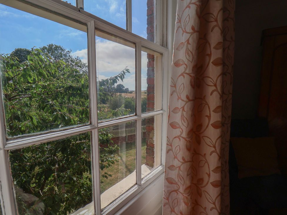 A view from a window with a curtain and trees outside at Reighton House in Reighton near Filey