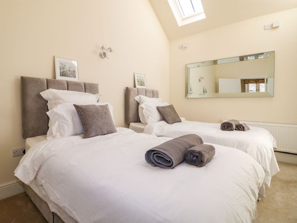 A bedroom with two beds, towels and a mirror at Churn Dash Cottage in Derby
