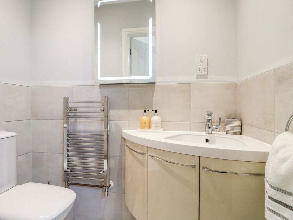 A bathroom with a sink, toilet, and a mirror at Churn Dash Cottage in Derby