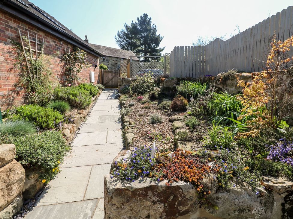 A garden with flower beds and a pathway at Churn Dash Cottage in Derby