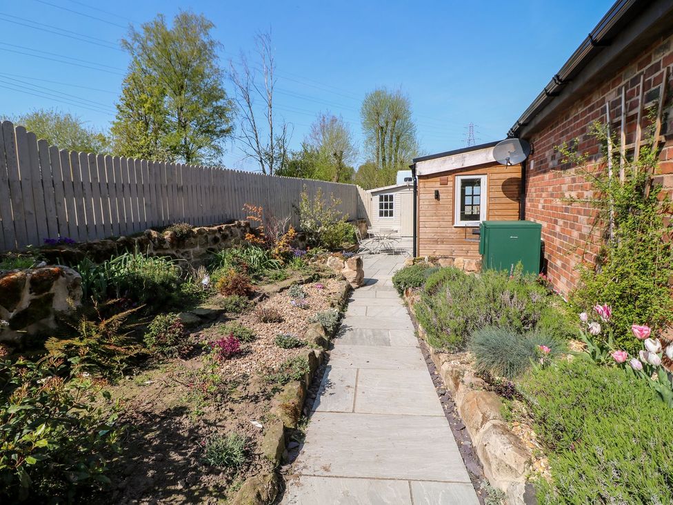 A pathway in a garden with a fence and flowers at Churn Dash Cottage Derby