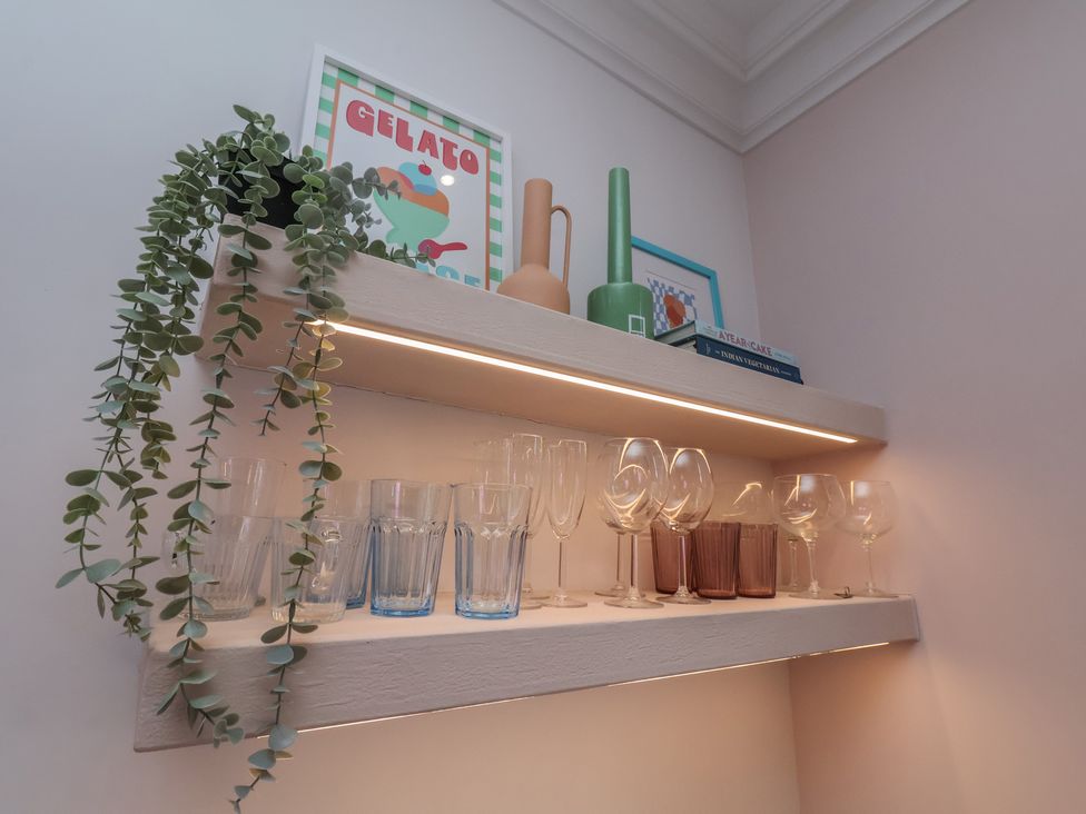 A kitchen shelf with glasses, plant, vases, and books at Apartment Pink