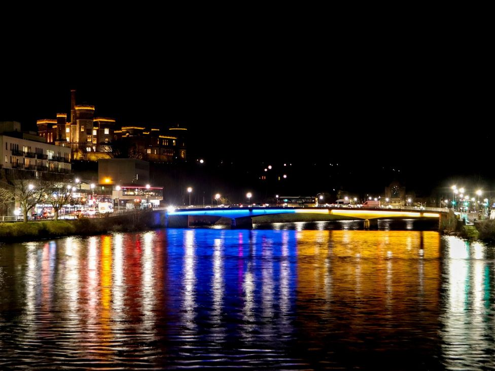 A view of a river with a bridge and illuminated buildings at 39 Knocknagael Inverness