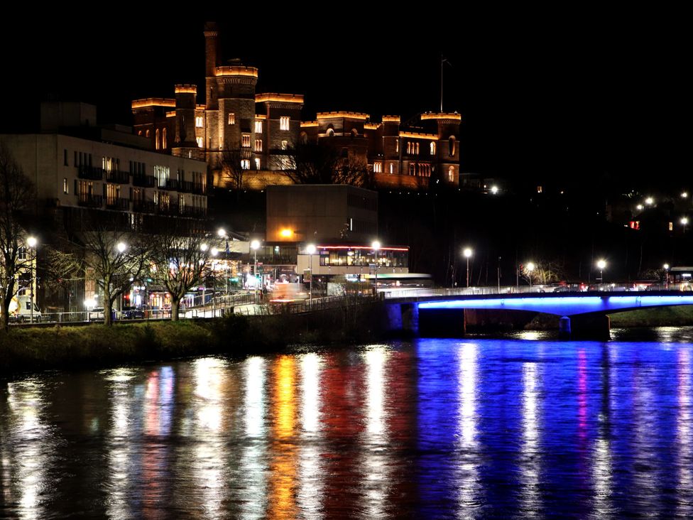 A night view of a castle and illuminated bridge over a river at 39 Knocknagael in Inverness