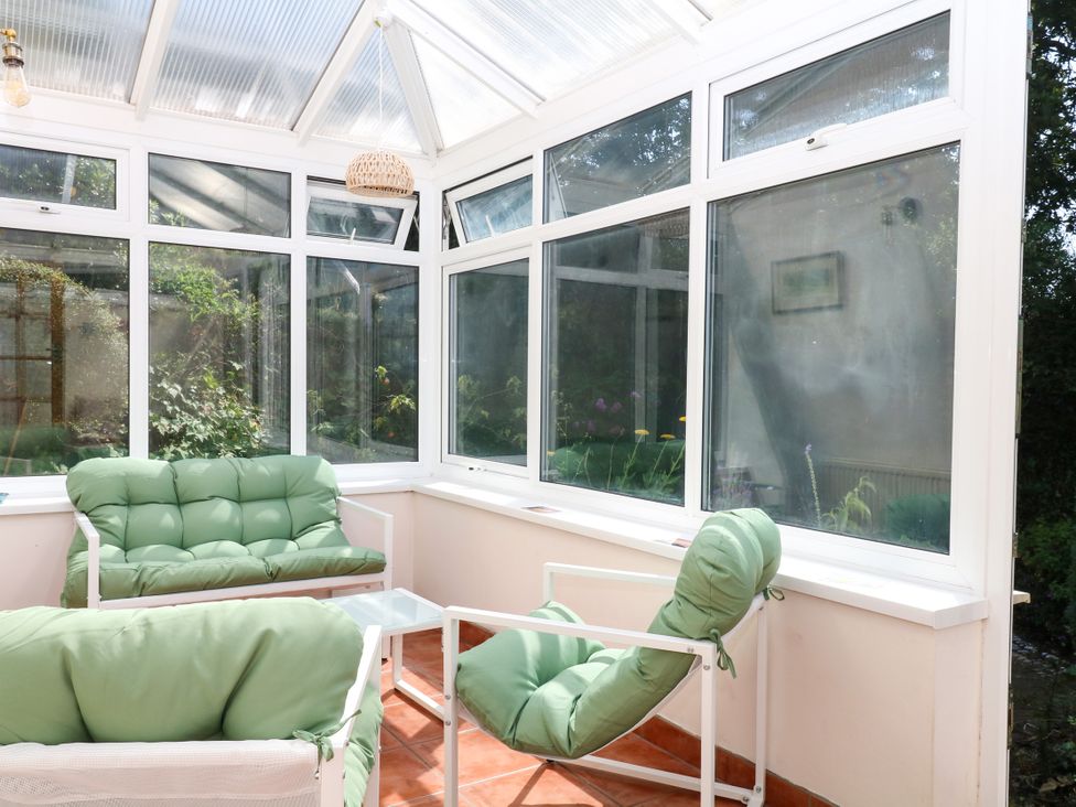 A conservatory with green sofas and glass windows at Gorway Cottage in Teignmouth