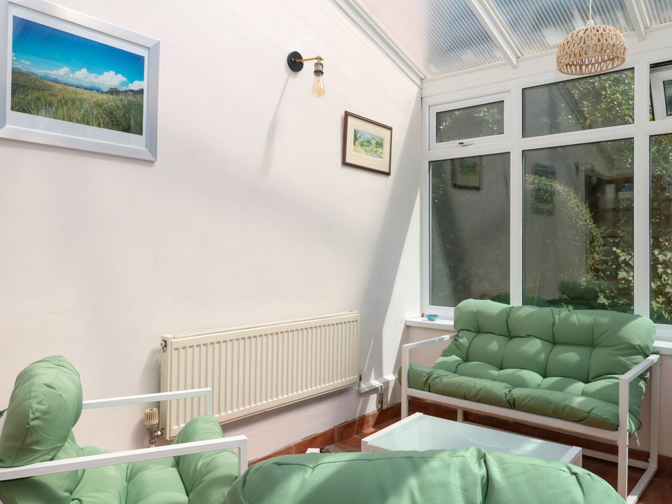 A conservatory with green sofas and a white table at Gorway Cottage in Teignmouth