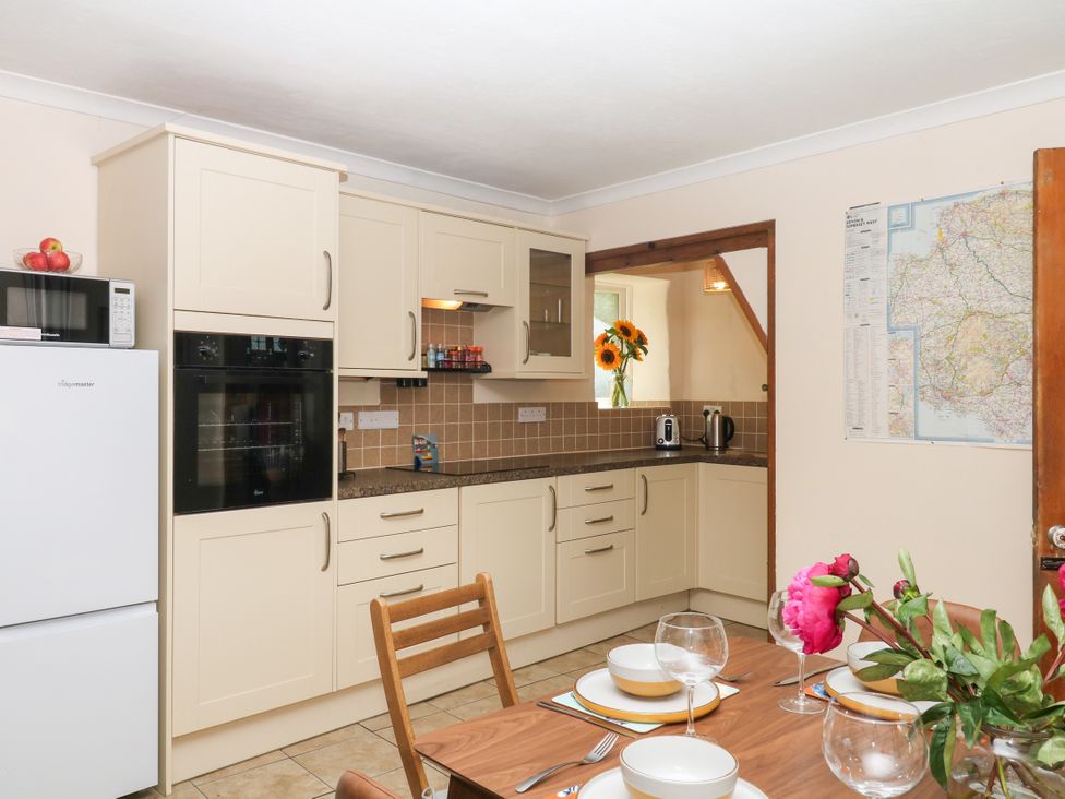 A kitchen with refrigerator, oven, sink, and dining table at Gorway Cottage in Teignmouth
