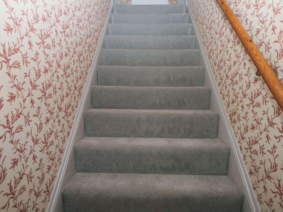 A staircase with grey carpet and floral wallpaper at Gorway Cottage in Teignmouth