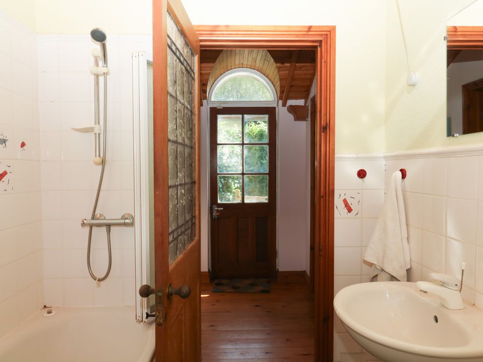 A bathroom with a shower, sink, and door at Gorway Cottage Teignmouth