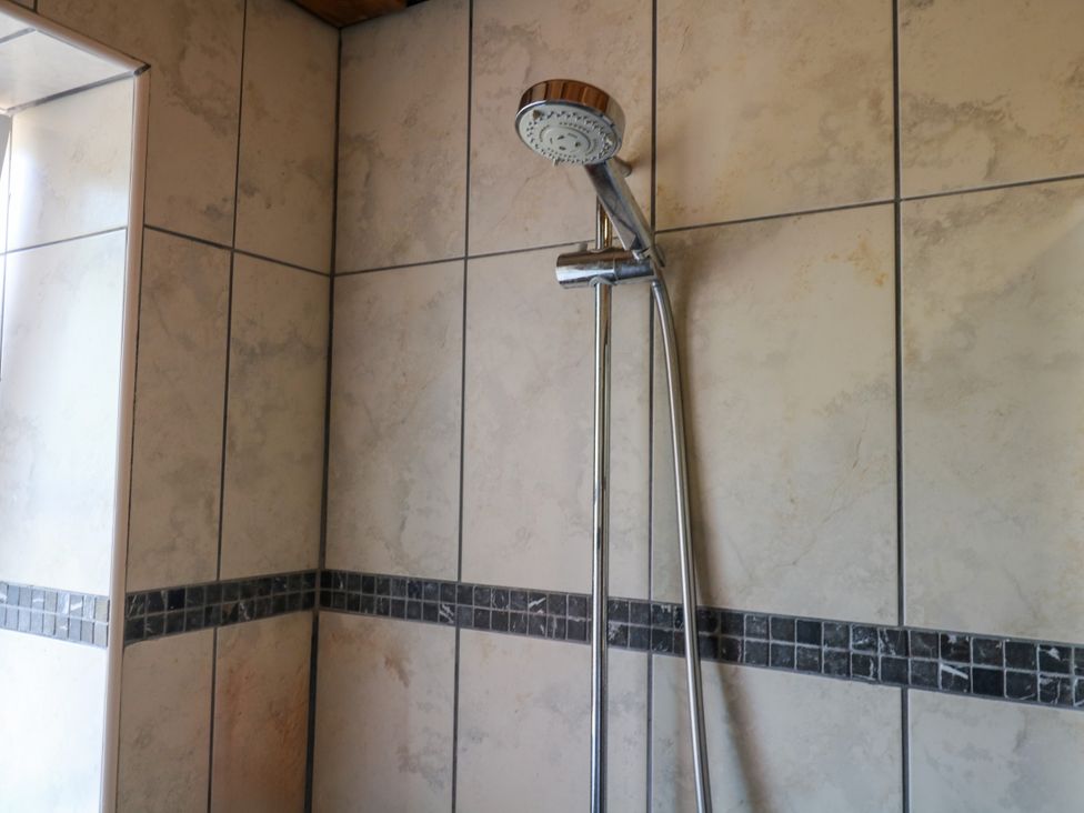 A shower head and wall tiles in the bathroom at Gorway Cottage Teignmouth