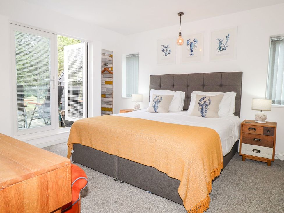 A bedroom with a bed, nightstand, and window at Seagull Shack in Morfa Bychan
