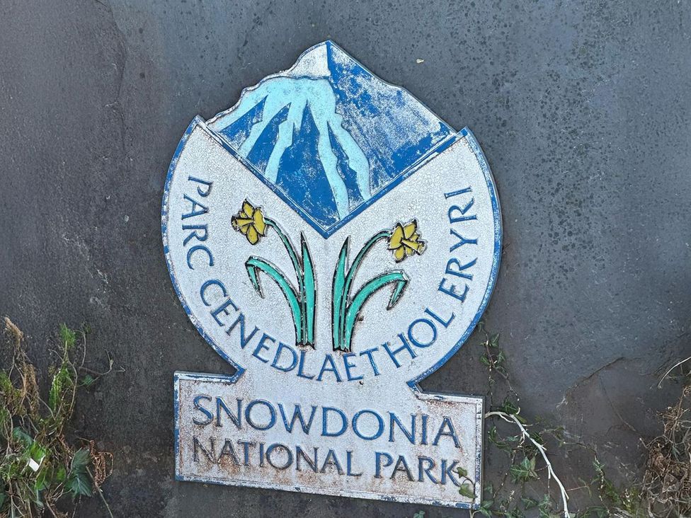 A sign for Snowdonia National Park with flowers at the base