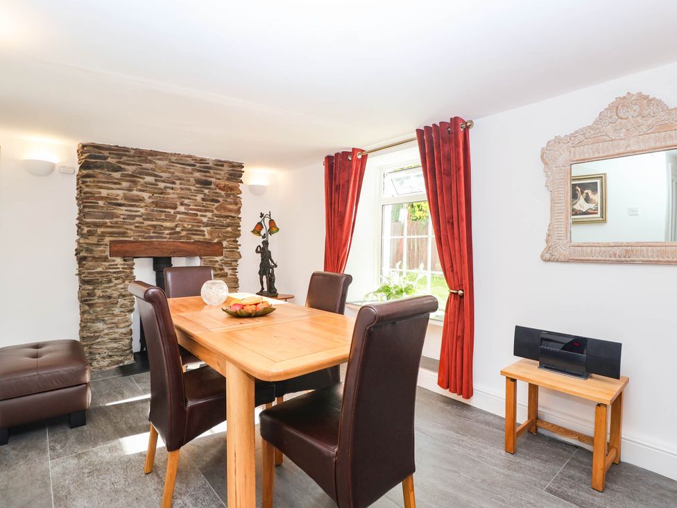 A dining room with a stone fireplace and wooden table at Swallow Cottage Sheviock near Crafthole
