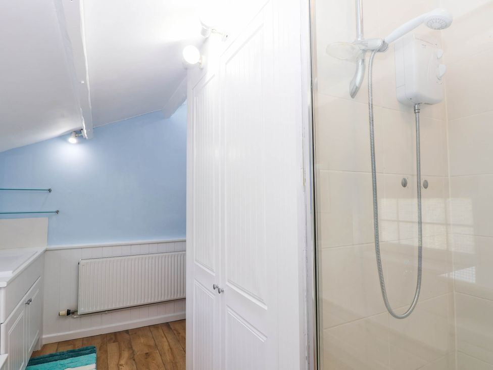 A bathroom with a shower, radiator, and shelf at Swallow Cottage in Sheviock near Crafthole