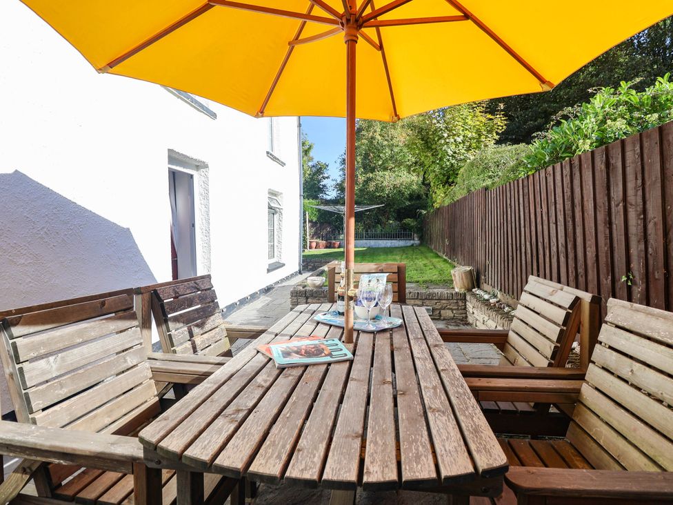 A garden with a table and chairs under an umbrella at Swallow Cottage in Sheviock near Crafthole