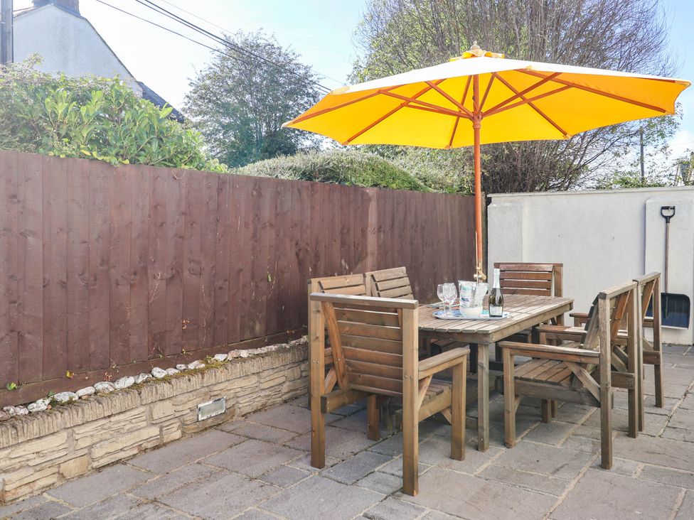 A garden with a wooden table and chairs under a yellow umbrella at Swallow Cottage in Sheviock near Crafthole