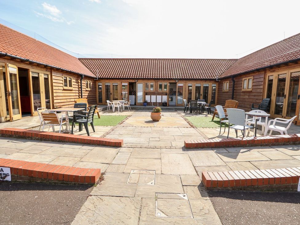 A courtyard with wooden buildings and seating areas at 5b Hideaways in Hunstanton