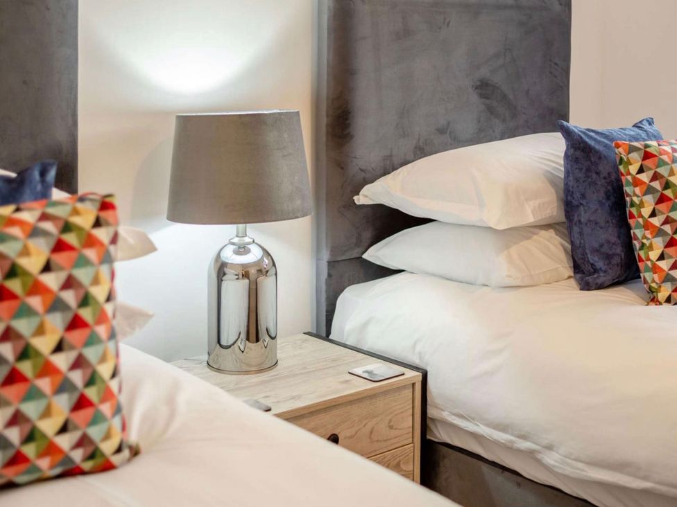 A bedroom with two beds and a lamp on a side table at Buttercup Cottage in Wadebridge