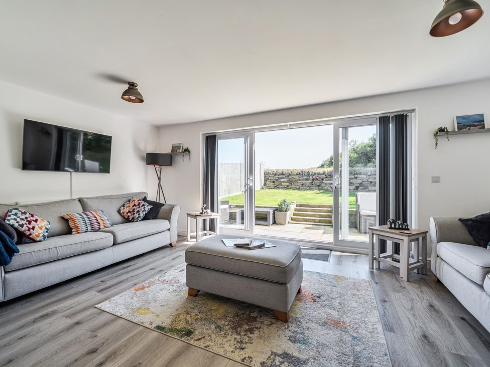A living room with a sofa and sliding doors to the outdoor area at Buttercup Cottage in St Merryn