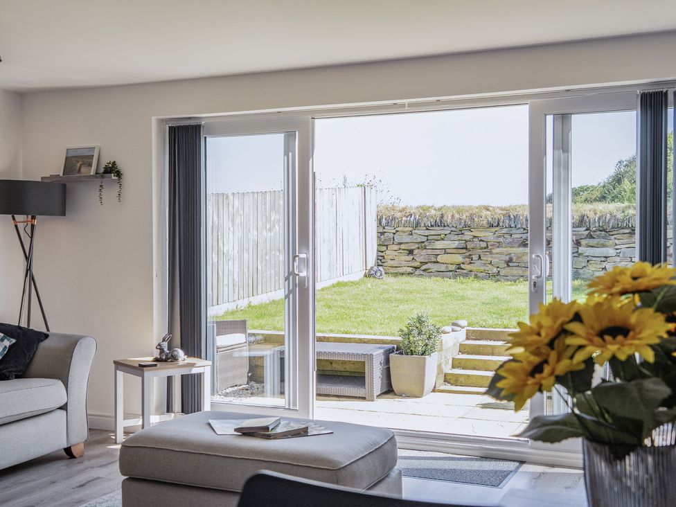 A living room with sliding doors opening to a garden at Buttercup Cottage in St Merryn